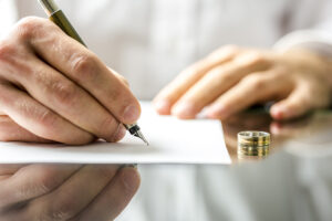 hands signing documents with wedding ring on table