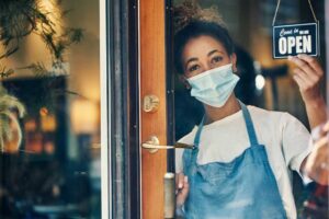 woman looking out window of store with open sign